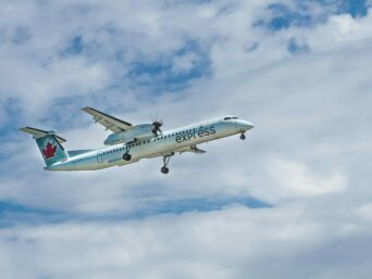 An Air Canada Express De Havilland Dash 8-400 climbs steadily through a cloudy blue sky. This modern turboprop aircraft is a staple of regional aviation, connecting smaller hubs with major international airports efficiently.